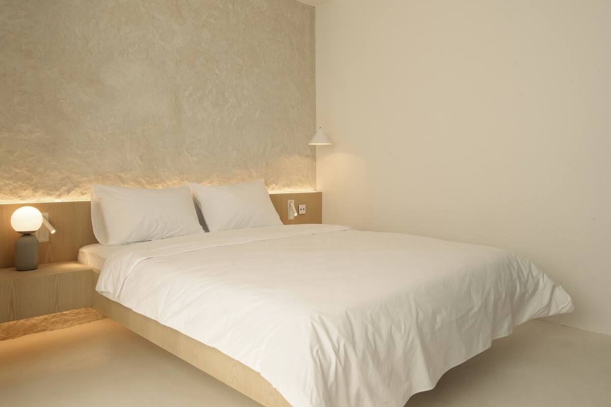 A minimalist bedroom with a large bed, two bedside tables with lamps, and a textured wall.