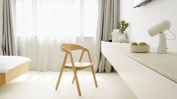 Ein schlicht eingerichtetes Hotelzimmer mit Bett, Schreibtisch mit Lampe, Stuhl und Wand-Fernseher.