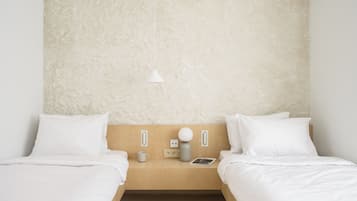 Habitación de hotel minimalista con dos camas individuales, cabecero de madera, mesita de noche con lámpara, una taza y un libro.