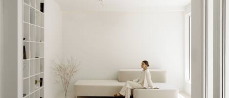 Un salón minimalista con un sofá blanco, una estantería empotrada y un jarrón con ramas secas.