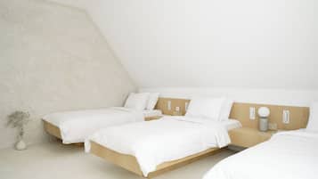 A modern bedroom with a sloped ceiling, two beds, a bedside table, and a vase with dried flowers.