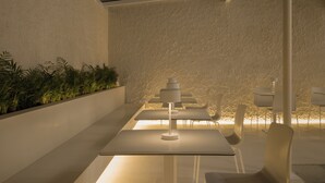 A modern interior with a dining area featuring white tables and chairs, a central white lamp, and a textured wall with a green plant wall. - Hotel Hello Plovdiv (Plovdiv)