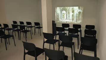 A room with rows of black chairs facing a large projection screen displaying an architectural image.