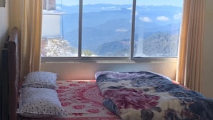 A bed with floral bedding, a window with a mountain view, and a curtain. - Yangzom La Homestay  (Gangtok)