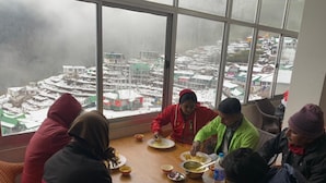 A group of people dining at a table with a view of a snowy landscape through large windows. - Yangzom La Homestay  (Gangtok)