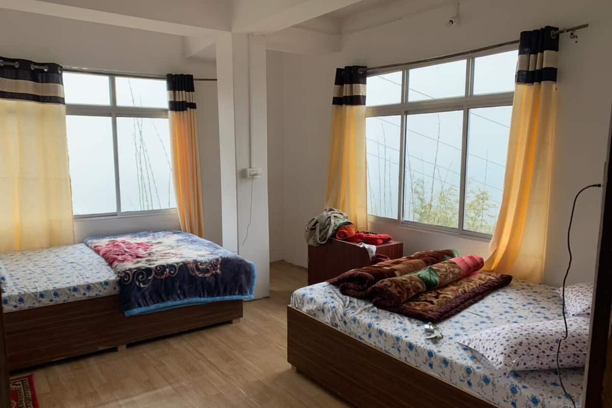 A room with two beds, wooden flooring, and large windows with curtains.