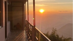 A balcony with a view of the sunset over a mountainous landscape. - Yangzom La Homestay  (Gangtok)