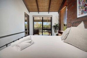 A bedroom with a bed, white towels, a balcony with a view, and a brick wall. - Coastal Dream | Bush Walks & Beach in Ocean Grove (Ocean Grove)
