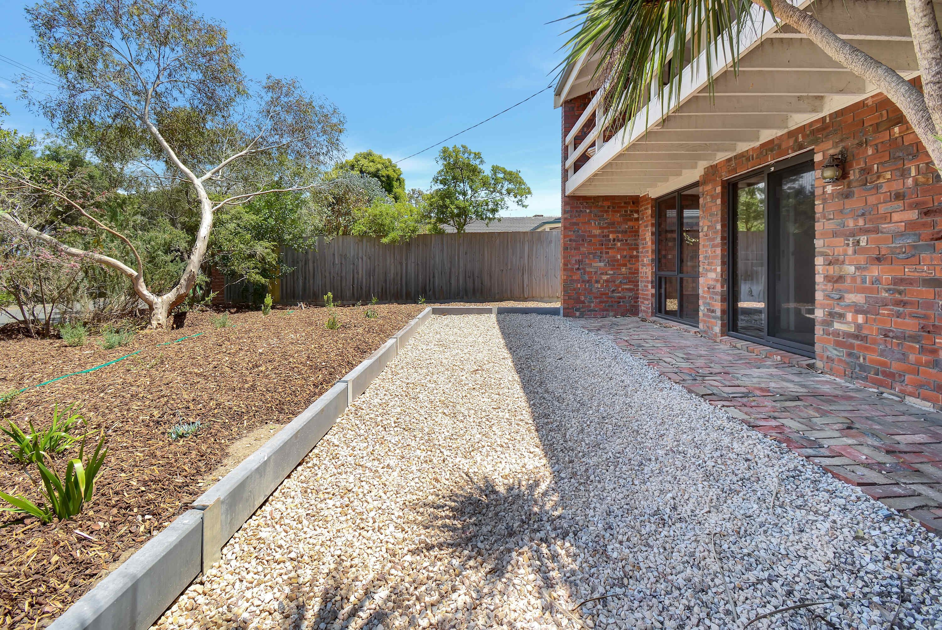 A backyard with a gravel pathway, a wooden fence, and a brick building with a balcony.