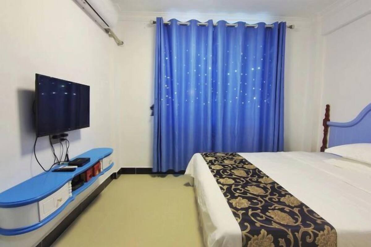 Une chambre d’hôtel avec un lit, un téléviseur posé sur un meuble, un rideau bleu et un mur bleu.