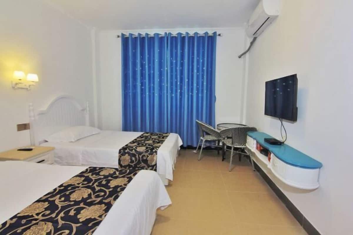Une chambre d’hôtel avec deux lits, une télévision, un bureau avec une chaise et une fenêtre avec des rideaux bleus.