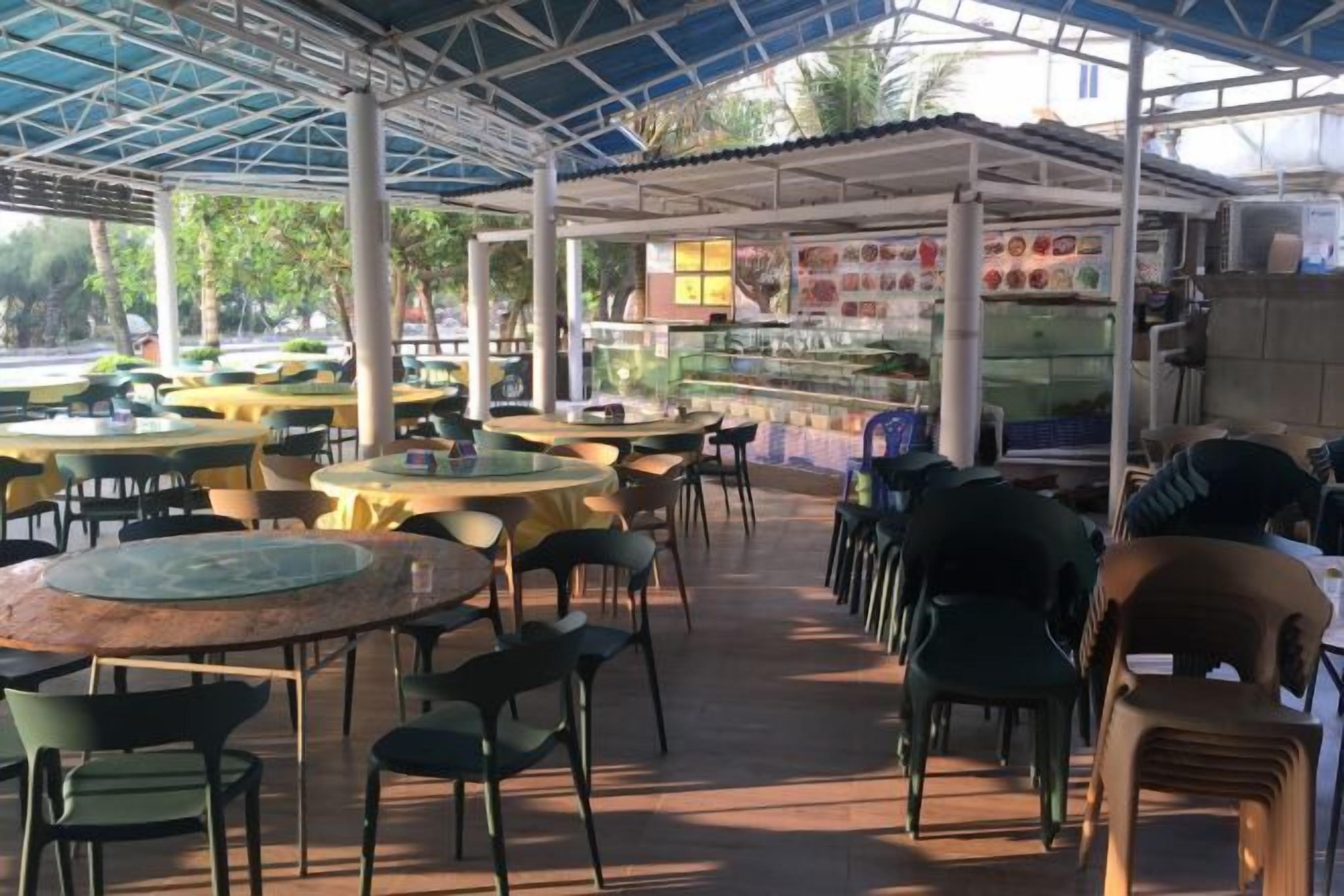 An outdoor cafe with round tables and chairs, a food display, and a covered seating area.