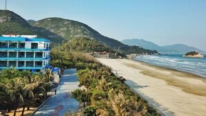 A coastal hotel with a blue building, a beach, and mountains in the background. - Jiaoyi Seaview Hotel (Taishan)