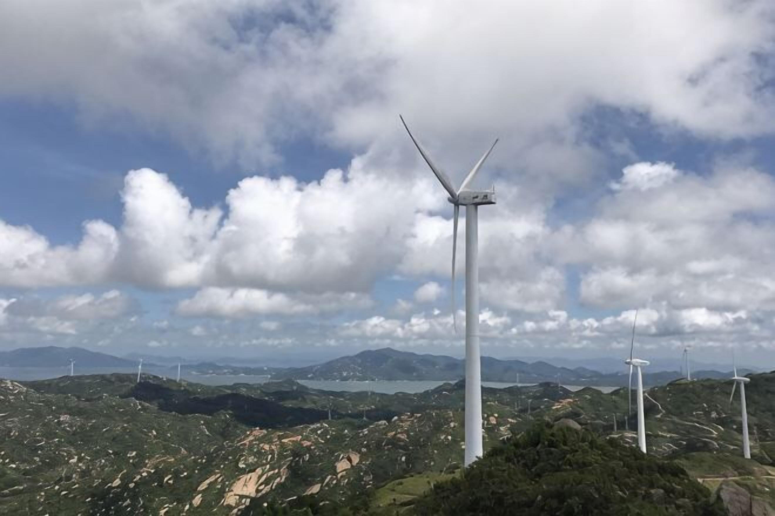 Eine Windturbine in einer hügeligen Landschaft, im Hintergrund weitere Turbinen.