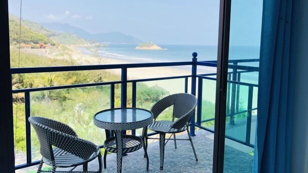 A balcony with two wicker chairs and a glass table, overlooking a beach and mountains. - Jiaoyi Seaview Hotel (Taishan)