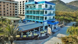 A multi-story hotel with a blue and white facade, outdoor seating area, and a view of surrounding hills. - Jiaoyi Seaview Hotel (Taishan)