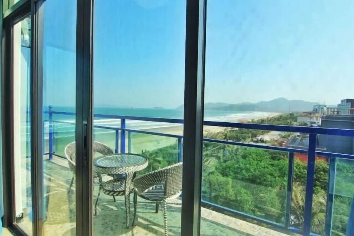 Un balcon avec une table et des chaises, donnant sur une plage et une végétation luxuriante.