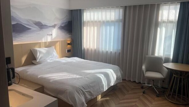 Hotelkamer met een bed, een bureau, een stoel en uitzicht op bergen door dunne gordijnen.