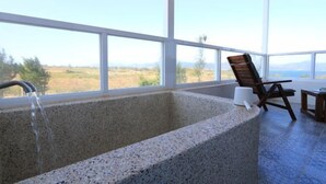 Zona d'spa amb una banyera gran, una cadira i vista al paisatge.