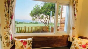 Habitació amb finestra que donava a una zona exterior tancada per una tanca, un banc de fusta i coixins amb motius florals.