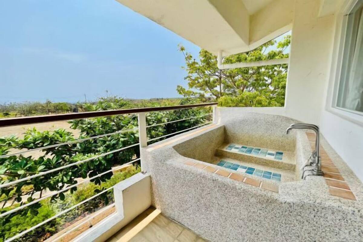 A balcony with a stone bathtub, a metal railing, and a view of greenery.