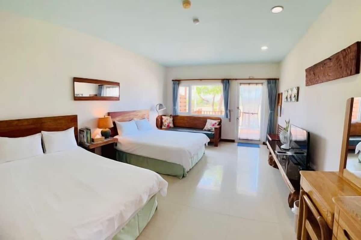 A hotel room with two beds, a TV, a desk, and a window with curtains.