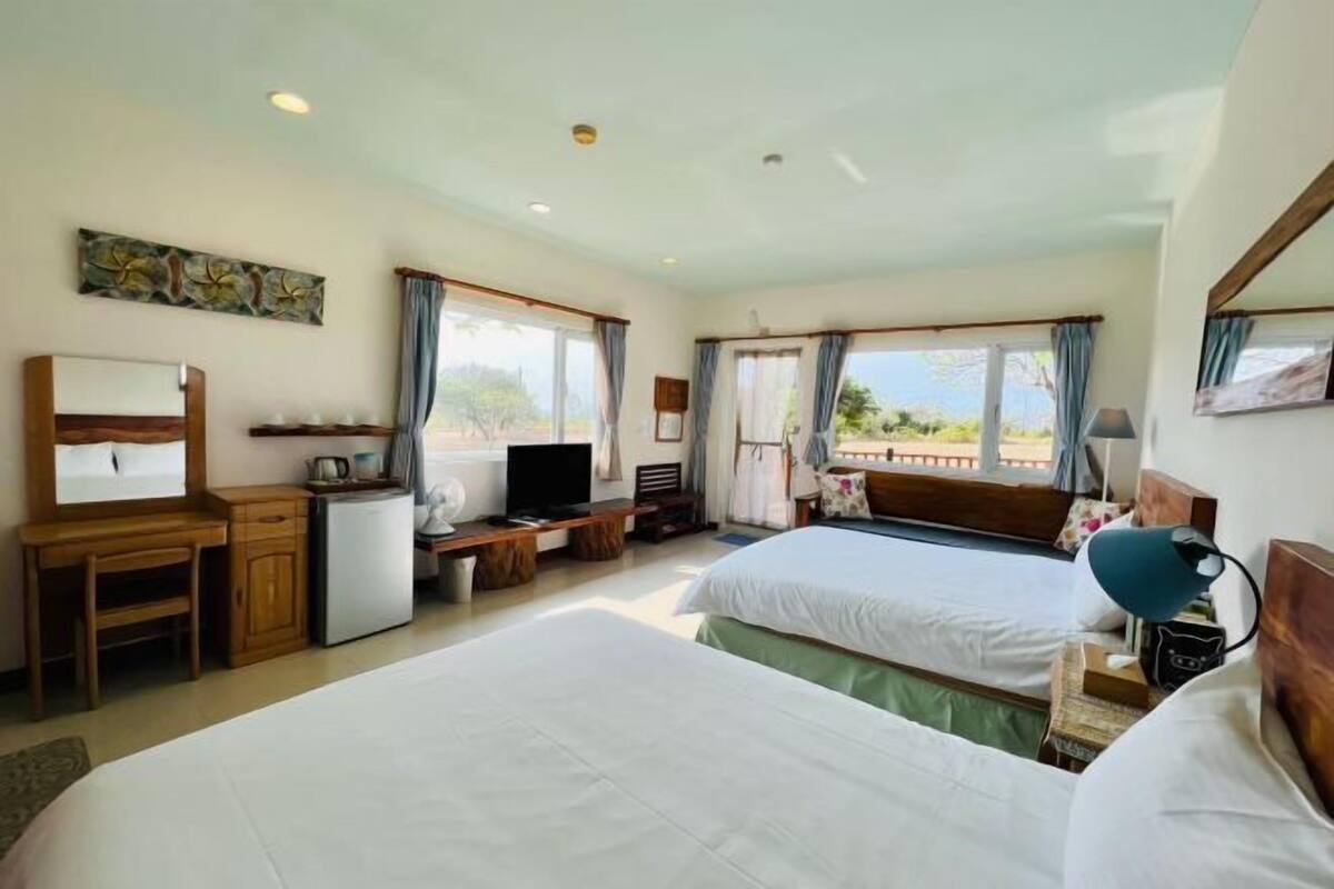 A hotel room with two beds, a desk, a television, and a view of the outdoors.