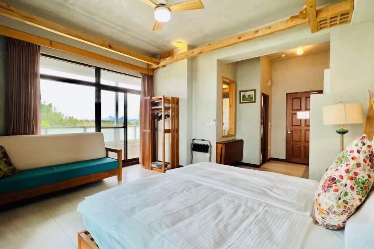 A bedroom with a bed, a sofa, a wooden wardrobe, a desk, and a window.