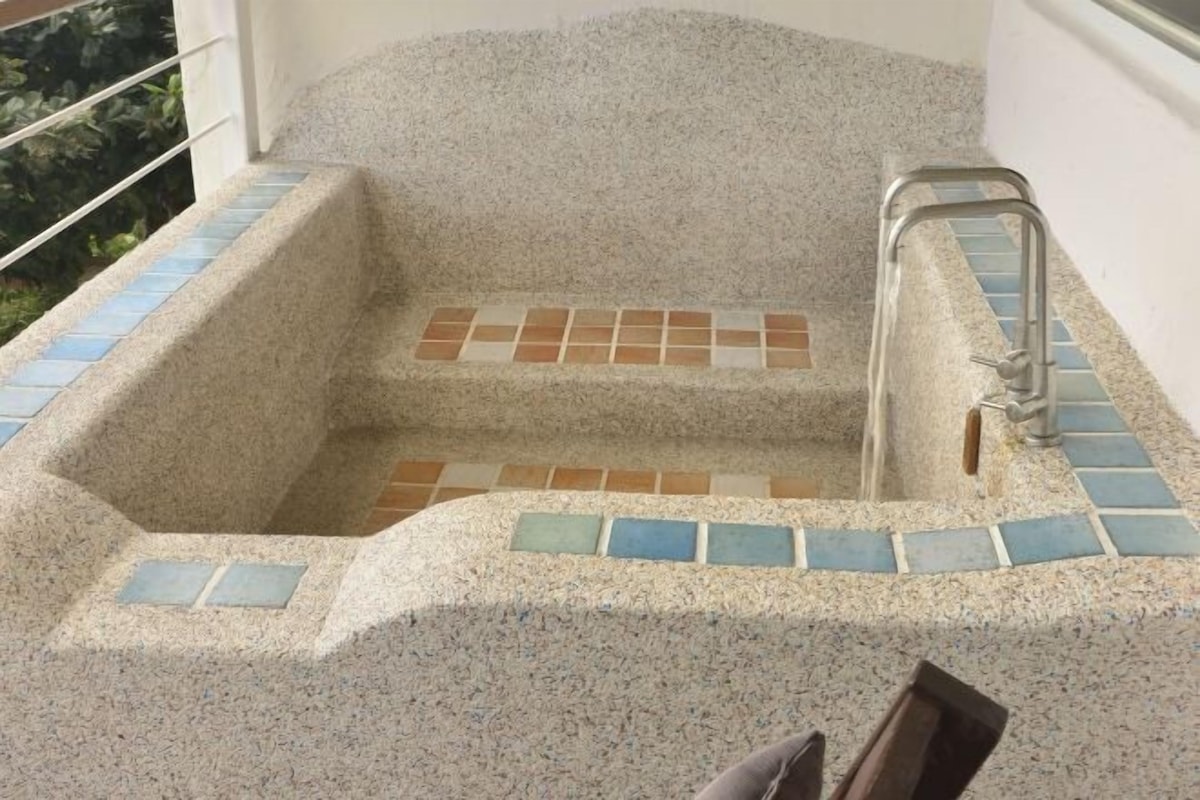 Une baignoire en pierre, avec un marchepied carrelé et une main courante en métal.