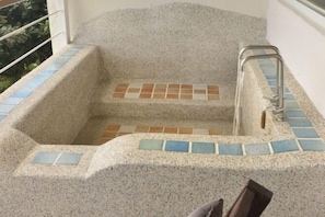 Une baignoire en pierre, avec un marchepied carrelé et une main courante en métal.