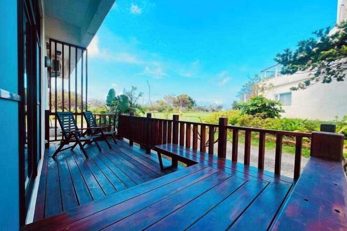 A wooden deck with a railing, a bench, and two lounge chairs.