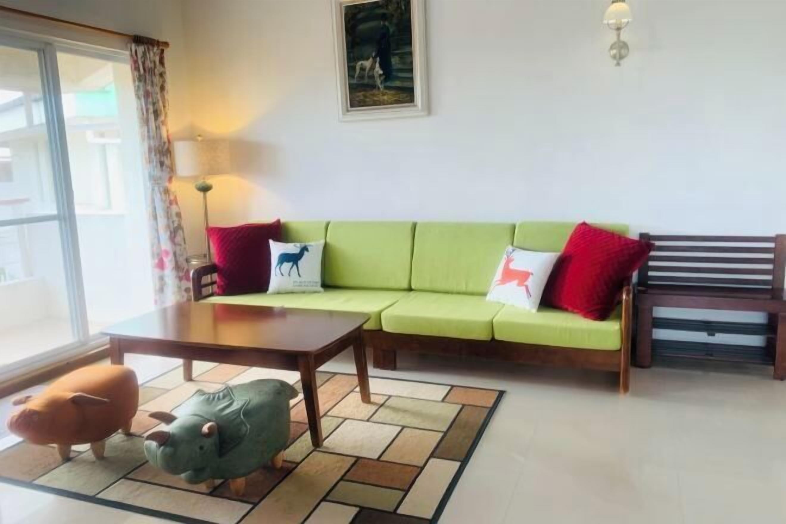 Uma sala de estar com um sofá verde, uma mesa de centro de madeira e duas almofadas em formato de animais.