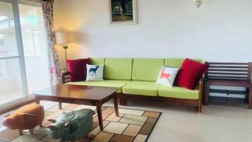 Uma sala de estar com um sofá verde, uma mesa de centro de madeira e duas almofadas em formato de animais.