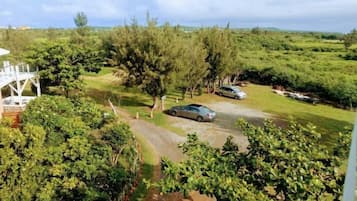Área residencial com um carro estacionado numa entrada, rodeada por vegetação exuberante e uma estrutura branca ao fundo.