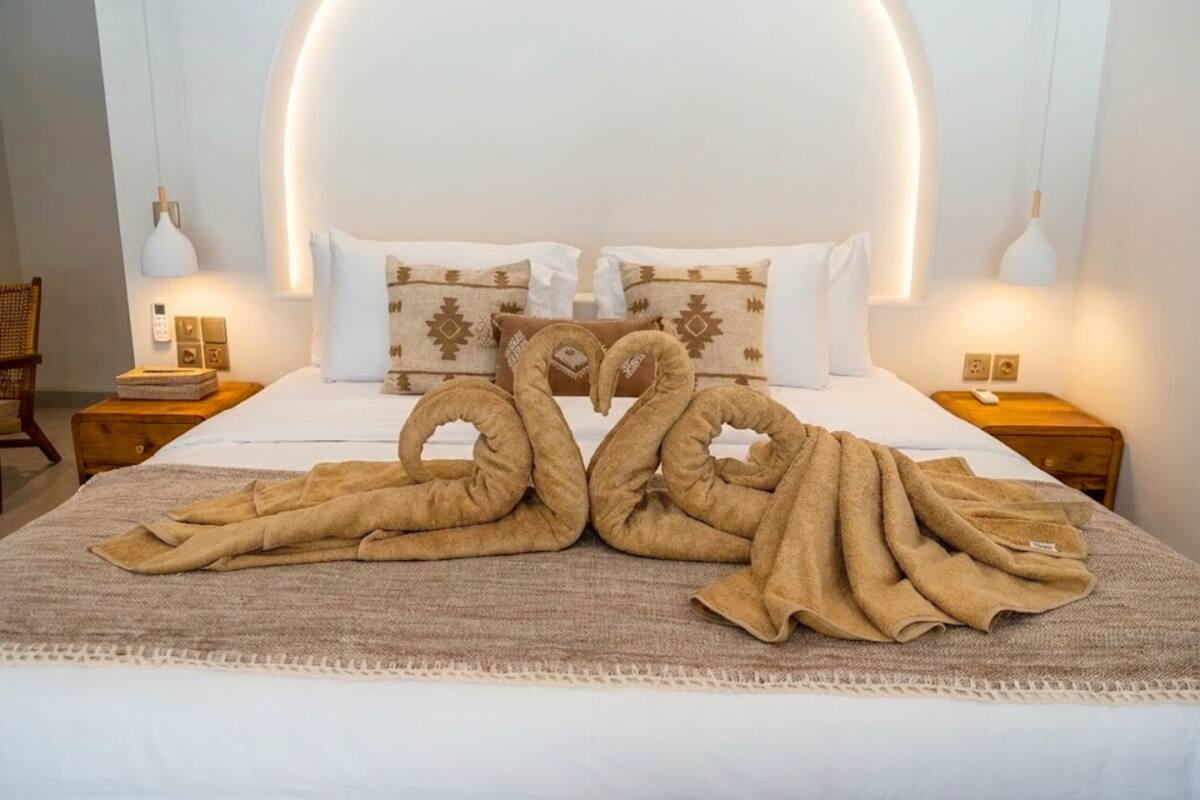 A neatly made bed with a unique swan-shaped towel arrangement, a white headboard, and bedside lamps.