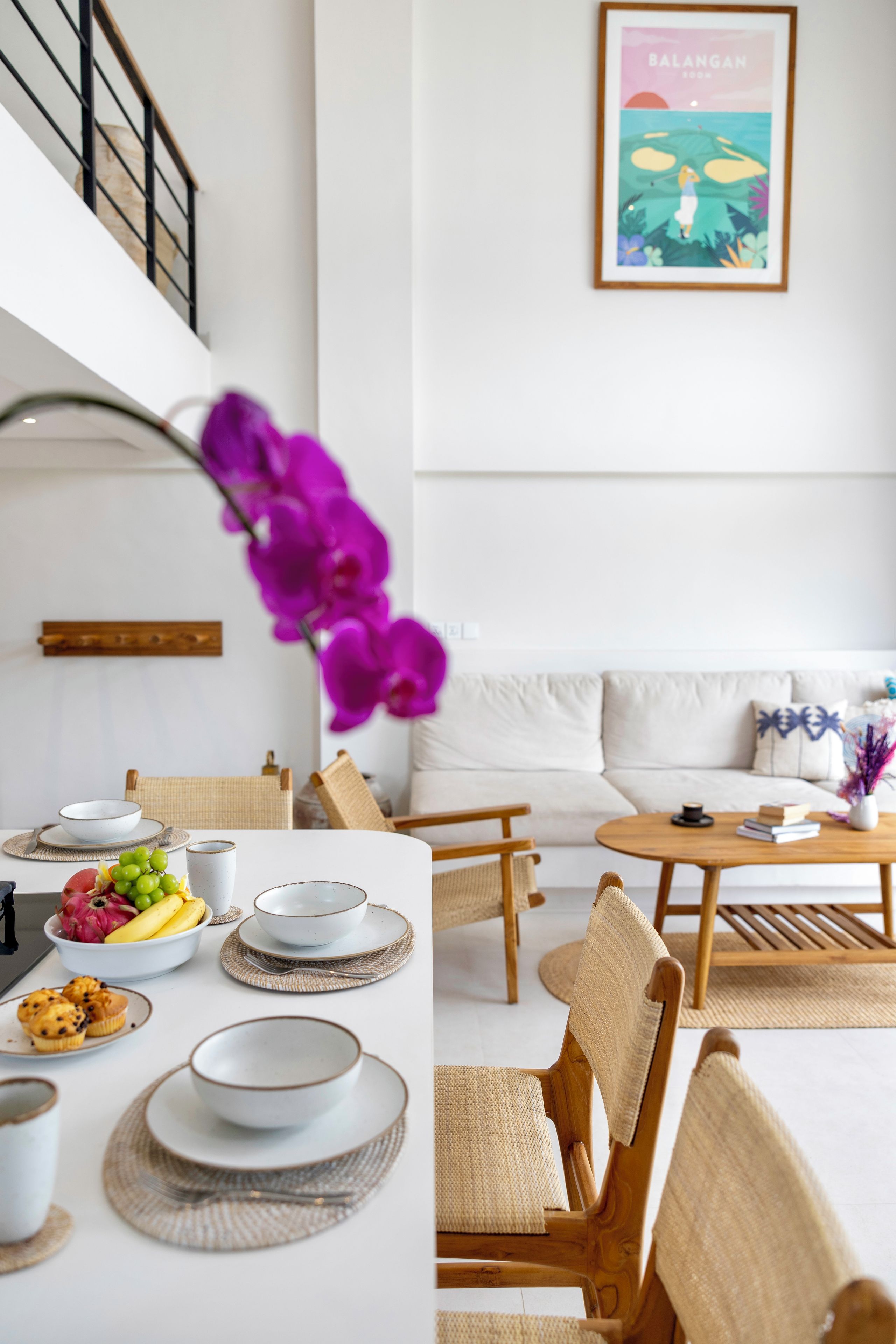 Una sala de estar moderna con comedor, que incluye una escalera, un sofá, una mesa de centro y un cuadro colgado en la pared.