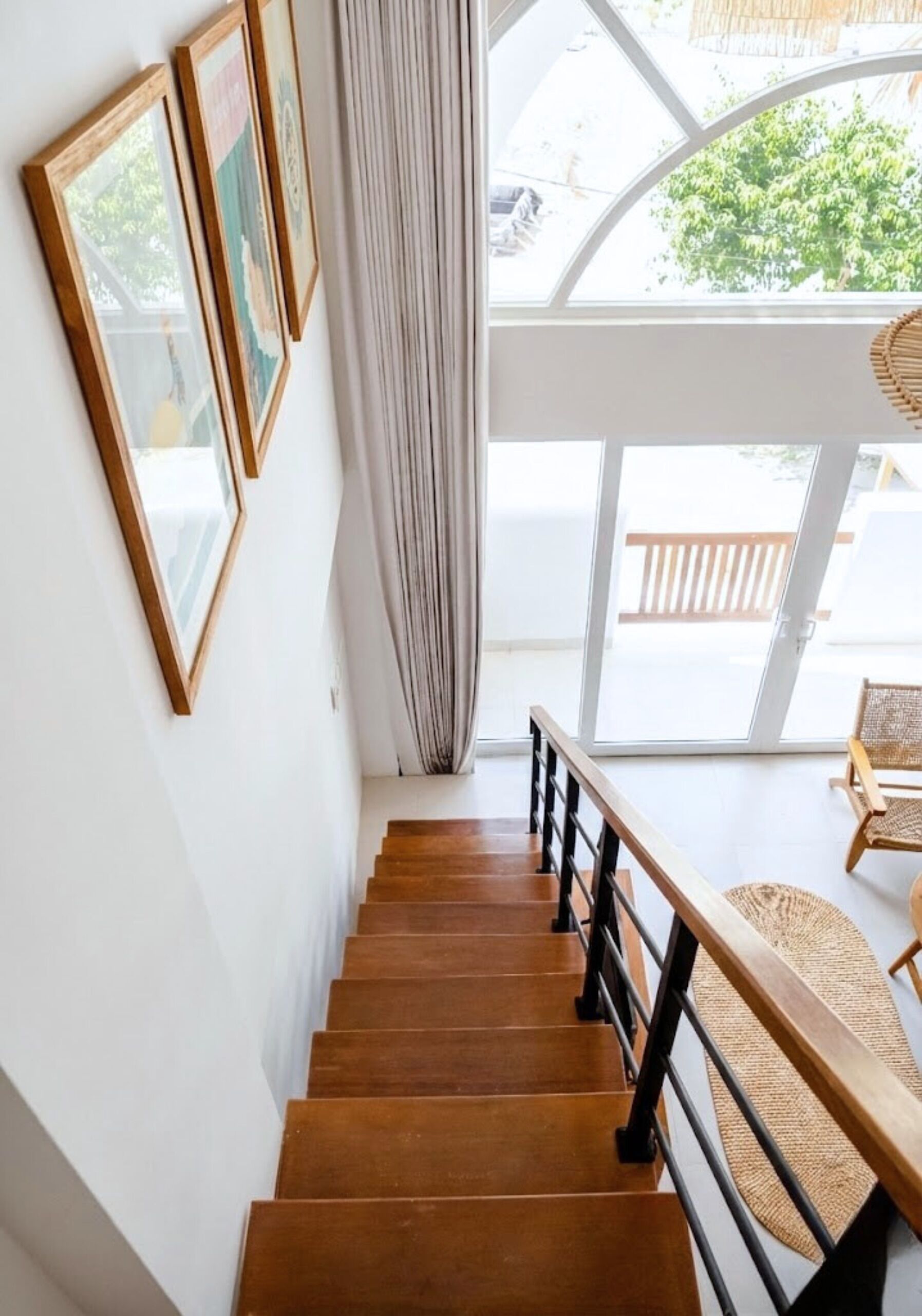 A wooden staircase with a black railing leading to a balcony with a wicker chair.