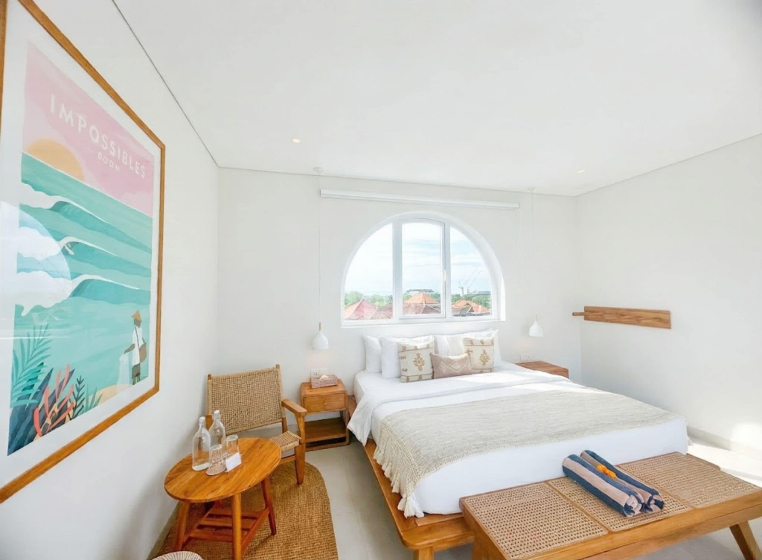 A bedroom with a large bed, a small table, a chair, a window with a view, and a wall-mounted shelf.