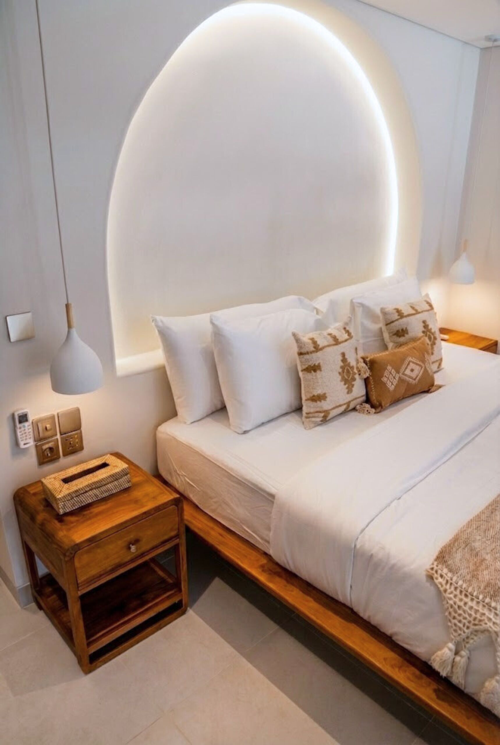 Quarto moderno com cama, mesas de cabeceira e luminária fixada na parede.