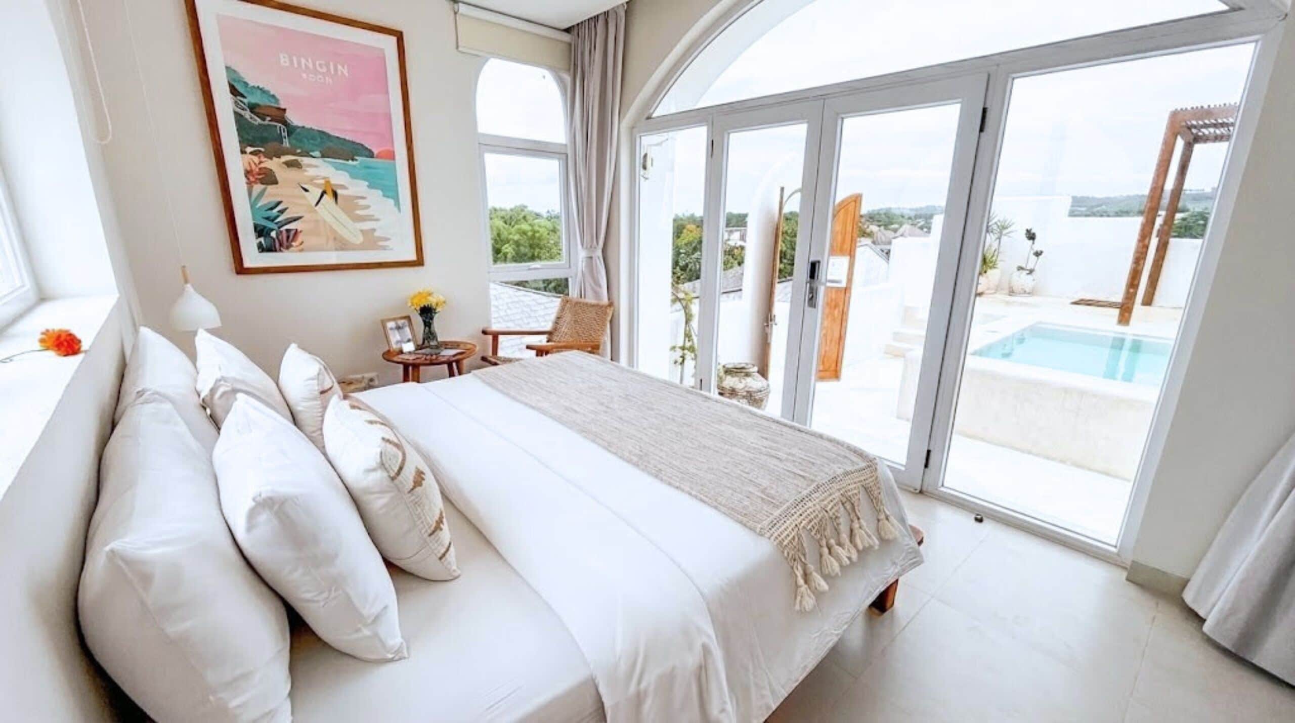 A bedroom with a large bed, a view of a swimming pool, and a poster on the wall.