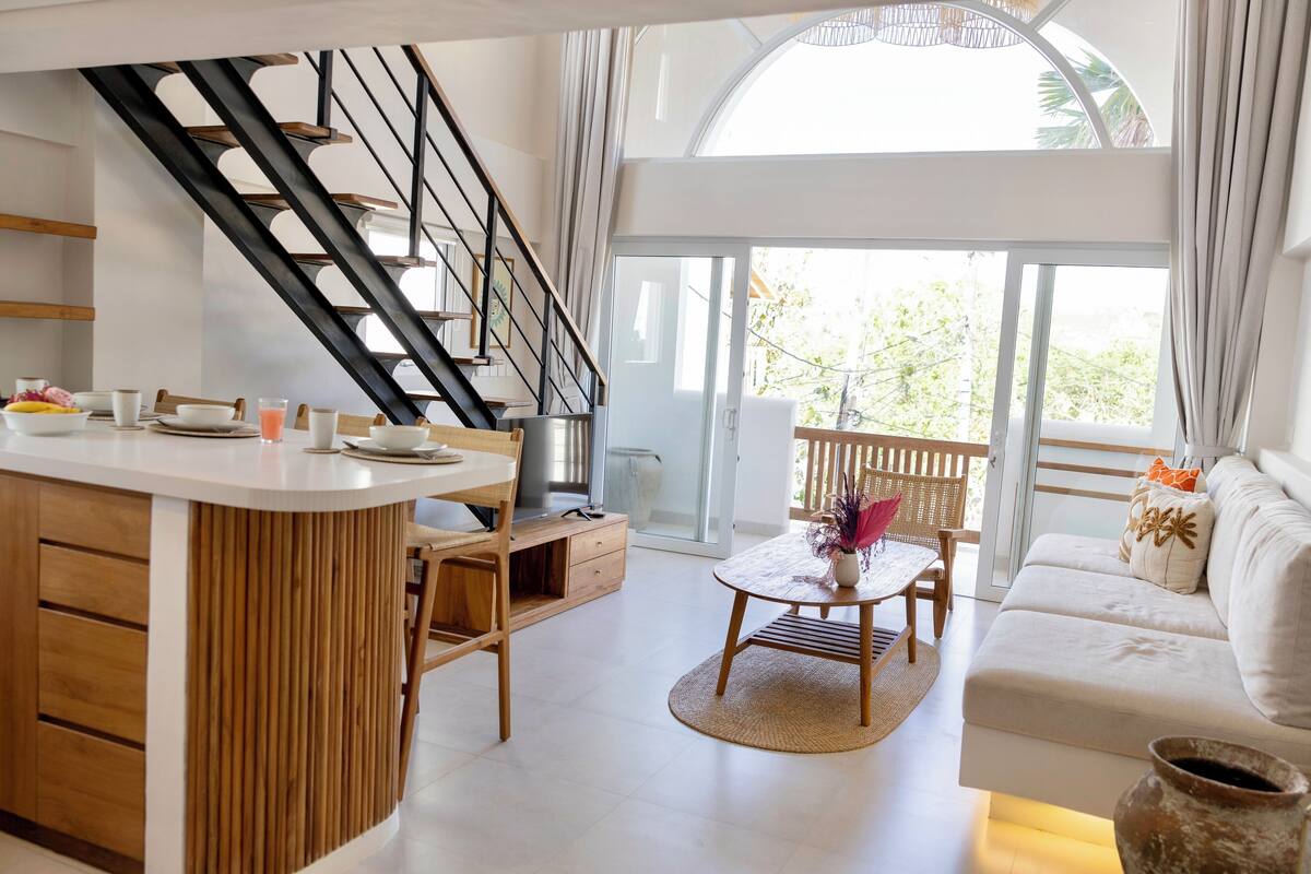 A modern kitchen with a central island, wooden cabinets, and a staircase.