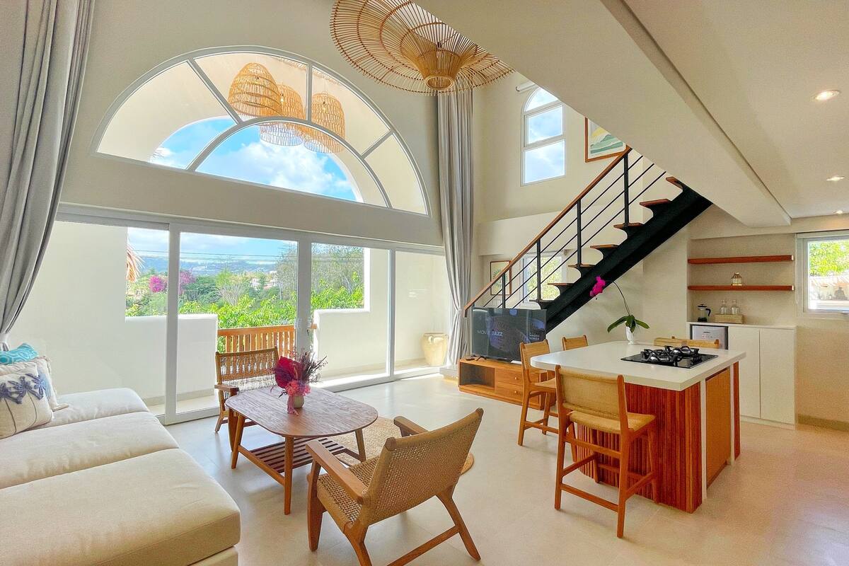 A spacious living area with a large window, a dining table, and a kitchen area with a gas stove.