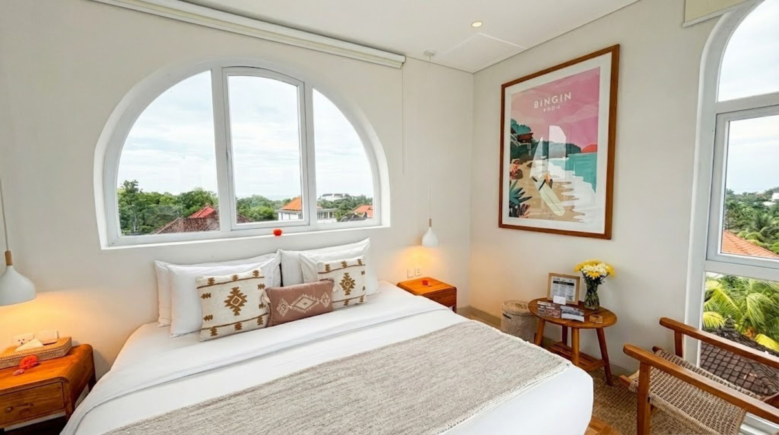 Un dormitorio con una cama grande, un ventanal con vistas, una mesita con lámpara y un cuadro en la pared.