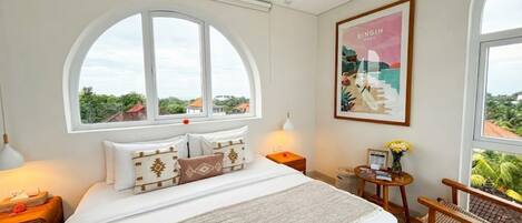 Un dormitorio con una cama grande, un ventanal con vistas, una mesita con lámpara y un cuadro en la pared.