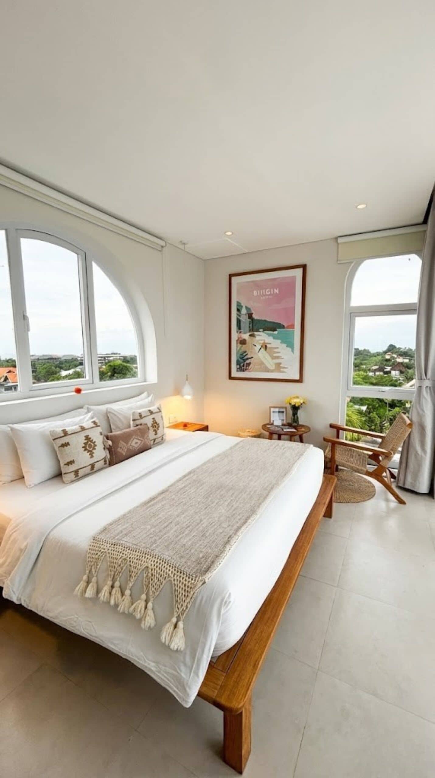 A bedroom with a large bed, a view of the outdoors, and a painting on the wall.