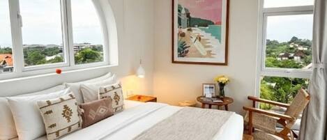 A bedroom with a large bed, a view of the outdoors, and a painting on the wall.