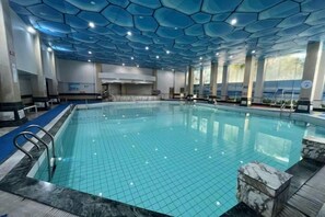 An indoor swimming pool with a tiled floor, a marble edge, and a ceiling with a geometric pattern. - New Century Hotel (Tongxiang)
