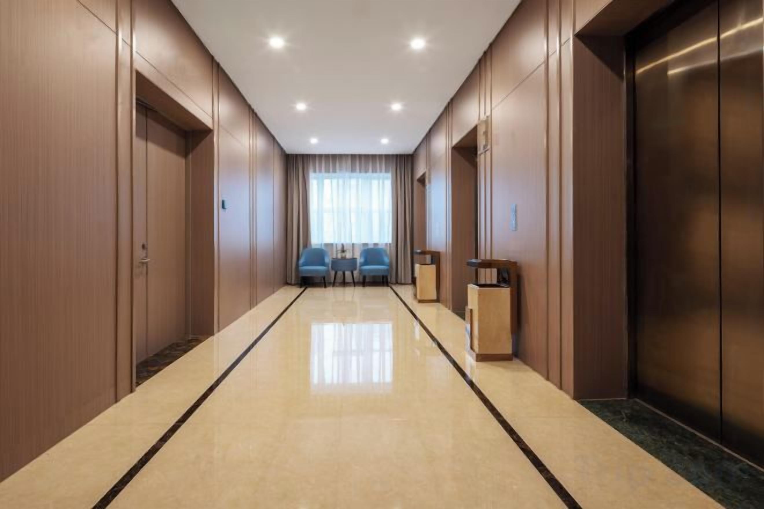 Un pasillo de hotel con piso pulido, paredes de madera y un ascensor a la derecha.