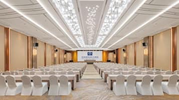 A conference room with rows of chairs, a stage, and a carpeted floor.