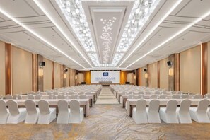 A conference room with rows of chairs, a stage, and a carpeted floor. - New Century Hotel (Tongxiang)